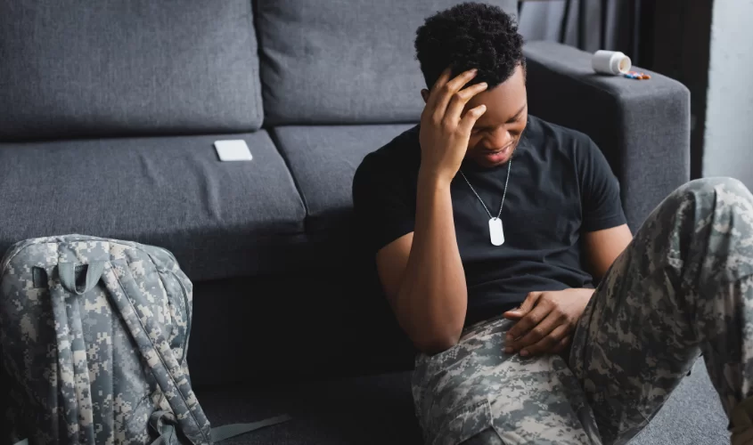 "Distressed soldier sitting on the floor in uniform with his hand on his head, symbolizing ptsd and the emotional toll of military service