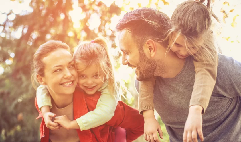 Happy family with parents giving piggyback rides to their smiling daughters outdoors