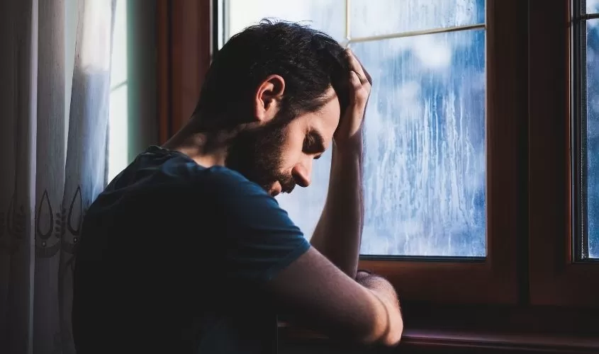 Man standing by window with hand on head