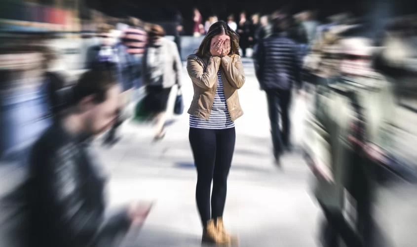 Woman in a public setting surround by lots of people with hand covering face symbolizing anxiety