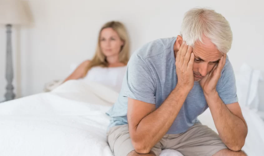 Man sitting on edge of bed frustrated with wife in bed behind him