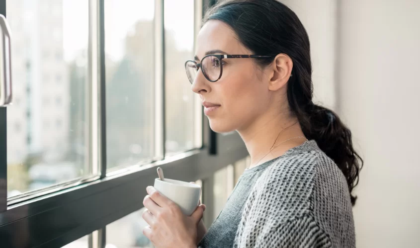 Woman looking out window with mug in hand