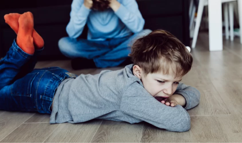 Child screaming on floor with parent behind him with head down