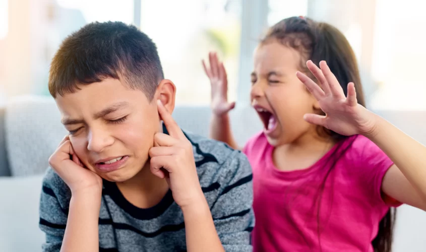Little girl screaming at brother. Boy plugging his ears, crying