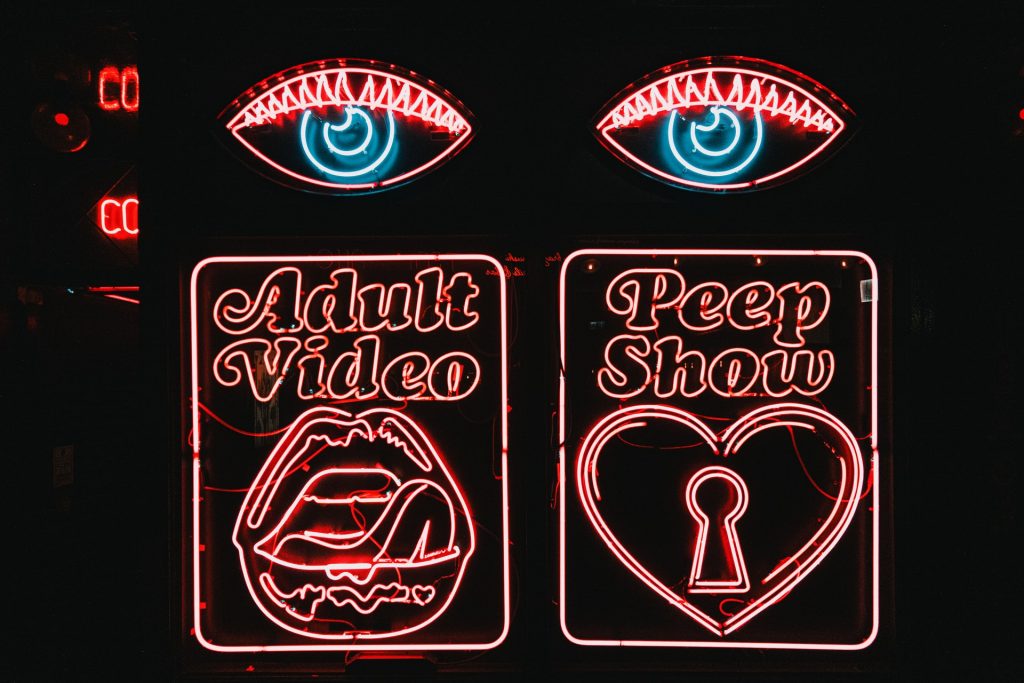 Neon sign on dark background with two eyes, advertising adult video and peep shows.