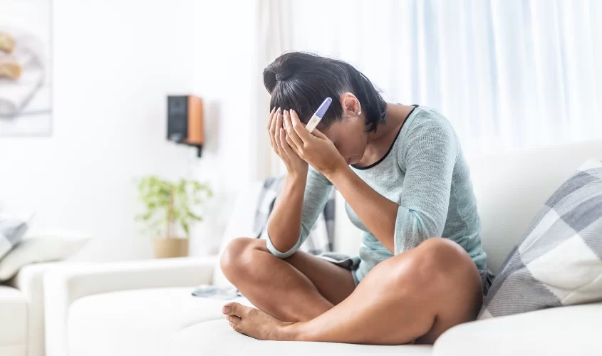Women upset with hand over head holding a pregnancy test