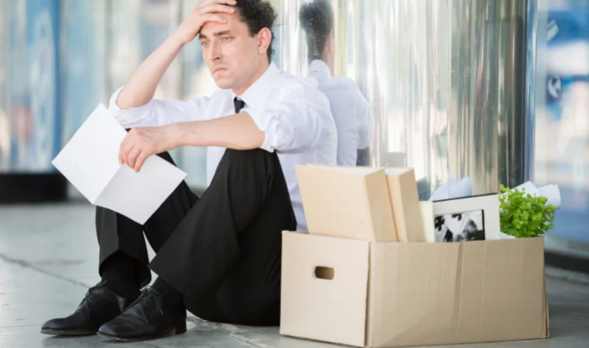 Man sitting on floor with box of belonging symbolizing loss of job