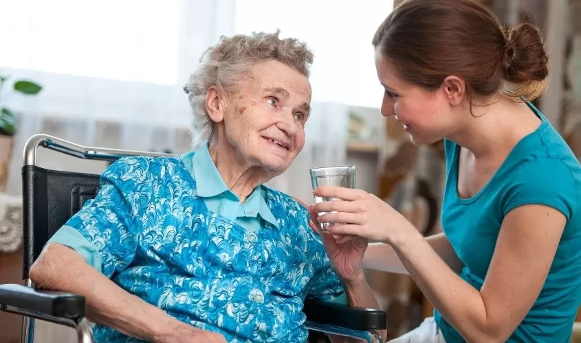 Young woman giving a glass of water to an older woman symbolizing care