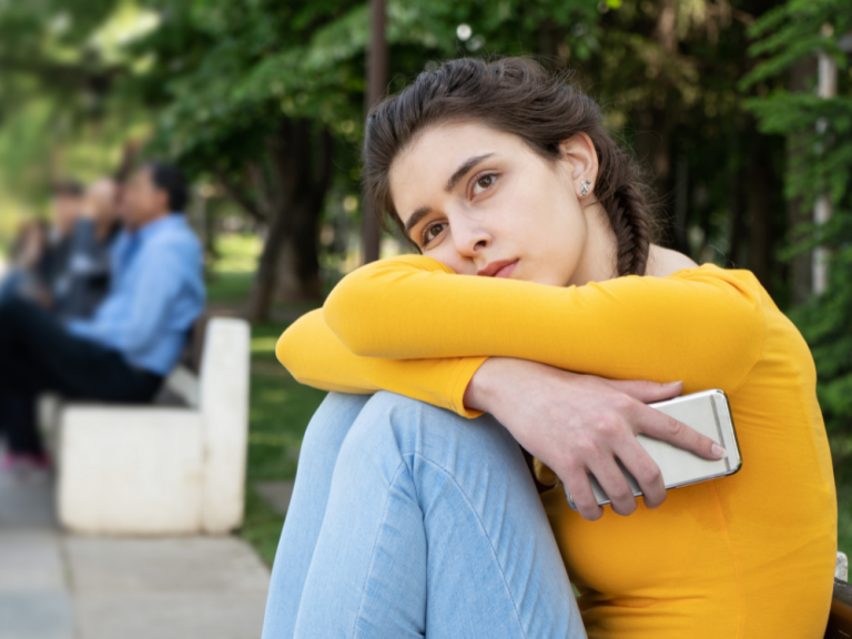 anxious teenager in yellow shirt with braided hair sitting with knees pulled up to chest
