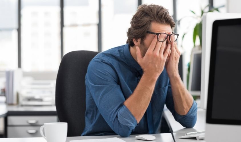 Stressed man at his desk rubbing his eyes in frustration