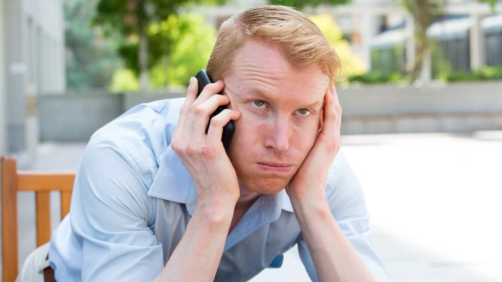 Frustrated man holding his head while on a phone call, sitting outdoors in a business shirt