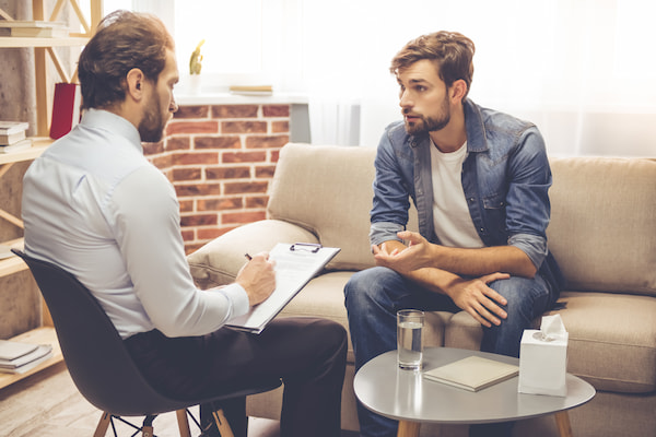 Man sitting on a couch talking to his male therapist