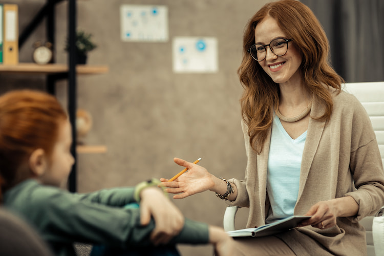 Experienced woman psychologist looking at her notes while having a session with a child