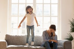 Happy Kid Jumping on a Couch with mom beside looking stressed