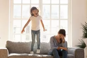 Happy Kid Jumping on a Couch with mom beside looking stressed