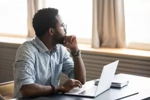 Thoughtful,African,American,Male,Employee,In,Glasses,Sit,At,Desk looking out the window