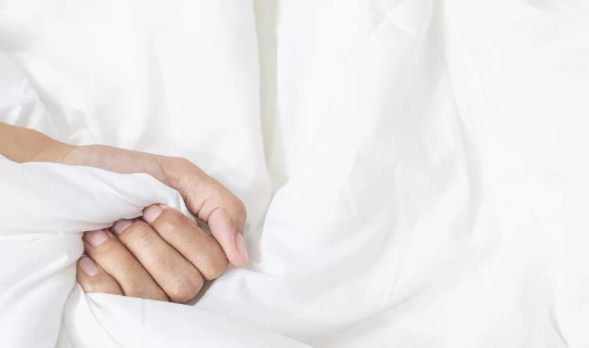 Person grasping sheets on a bed.