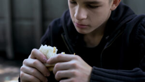 Hungry teen boy eating cheap unhealthy sandwich, poor quality meal for child