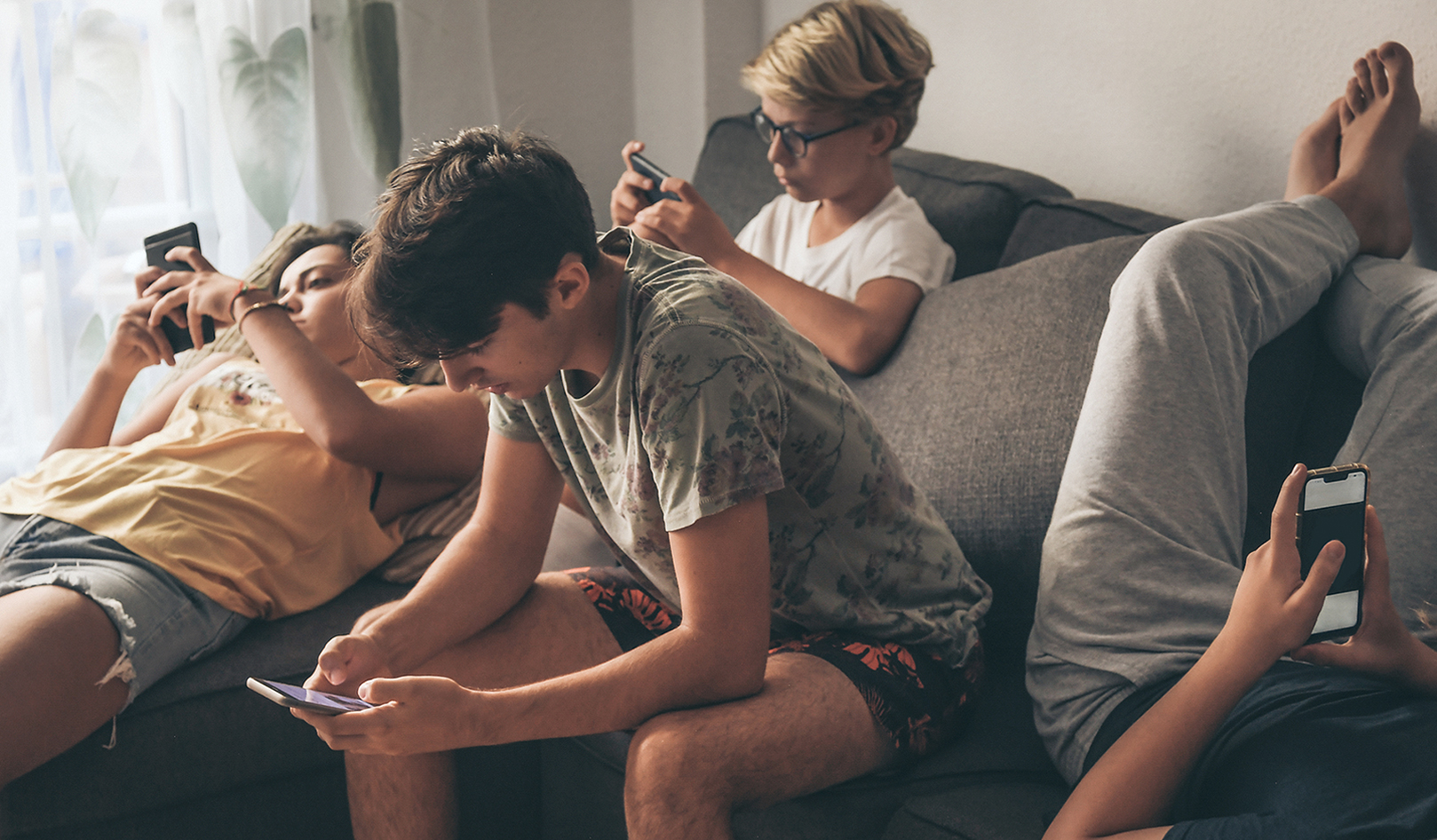 Kids sitting on a couch, each focused on their phones.