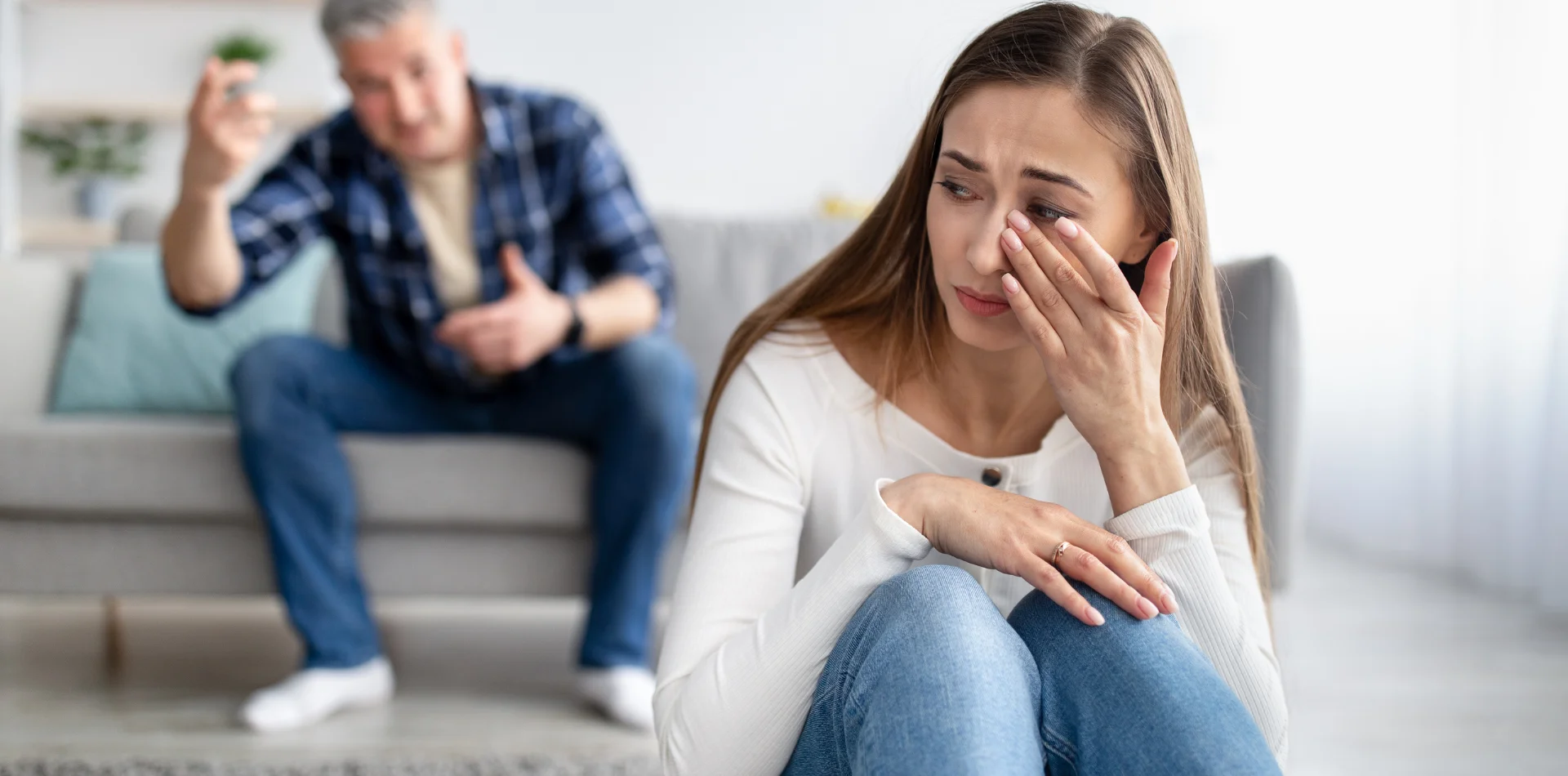 A woman wiping tears while a man gestures angrily in the background during an argument.