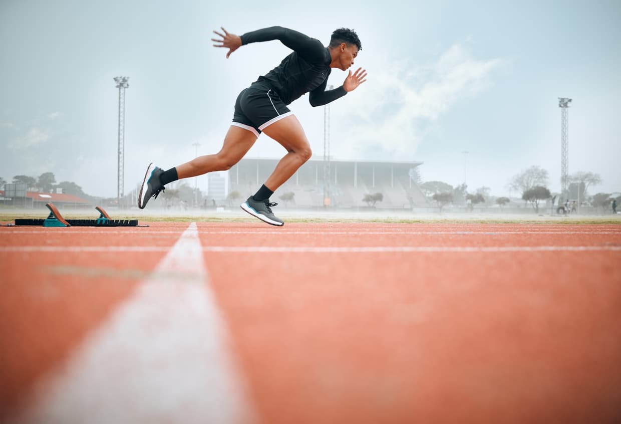 Young male sprinter explosively launching from starting blocks on an outdoor running track during athletic training or competition.