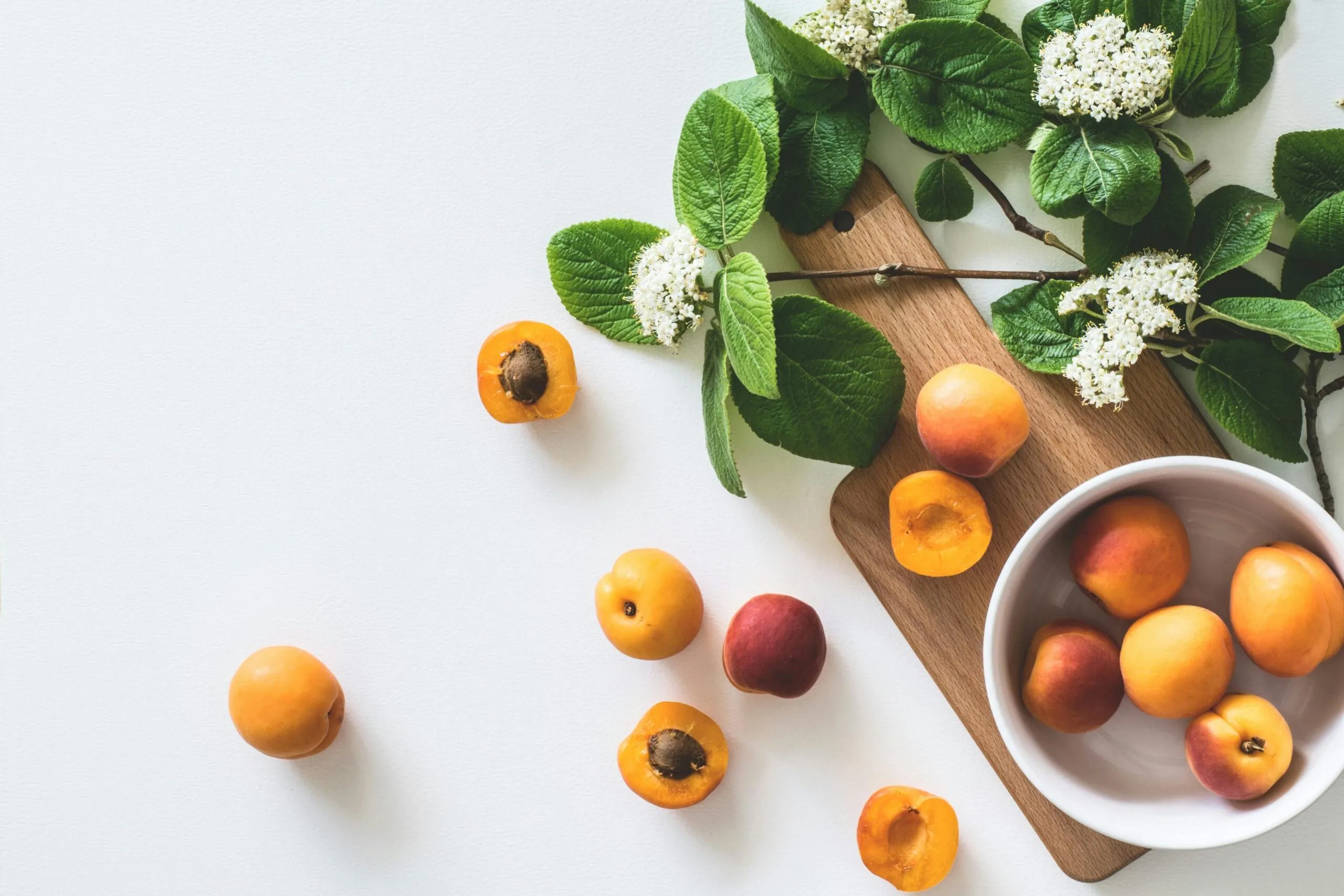 A flat lay of fresh apricots and blossoms on a board showcasing summer freshness.