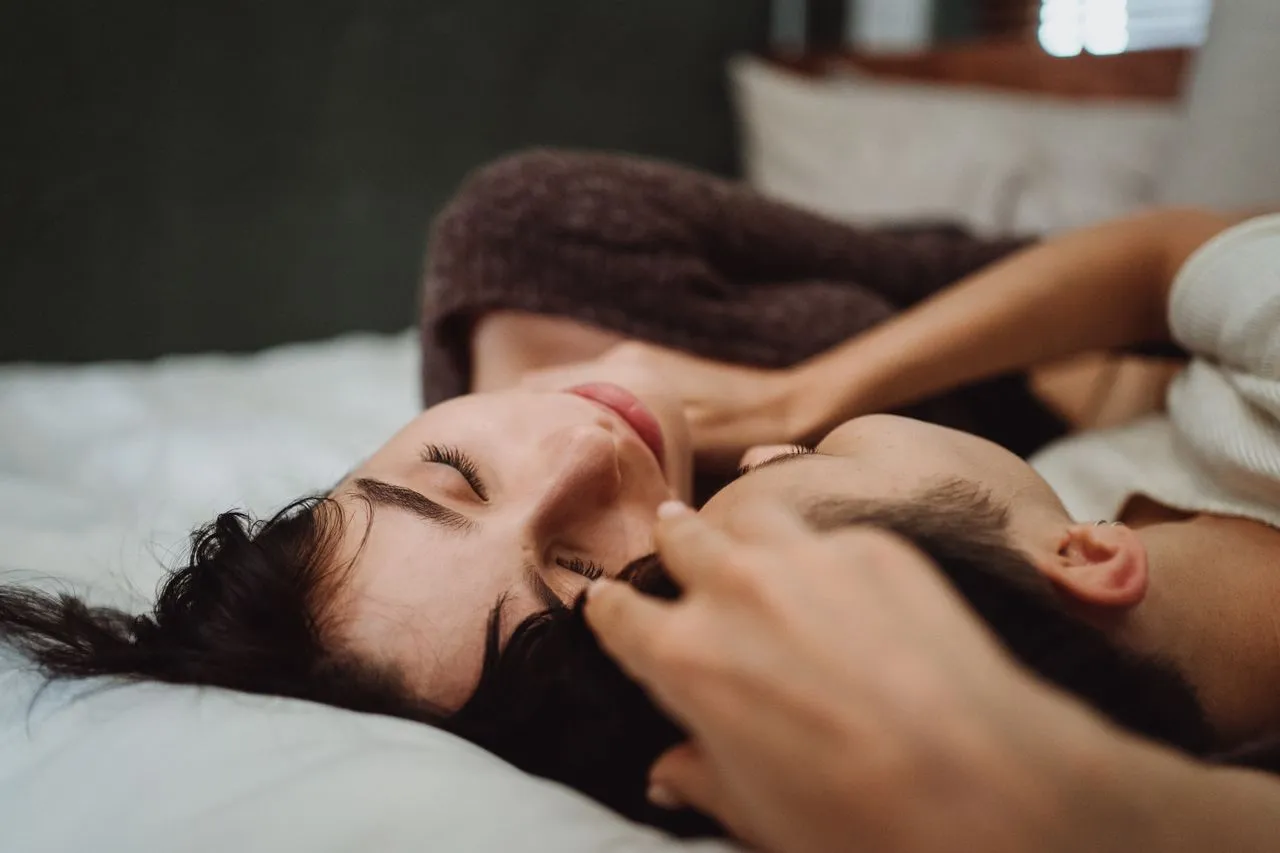 A close-up of two women embracing and resting peacefully together on a cozy bed.